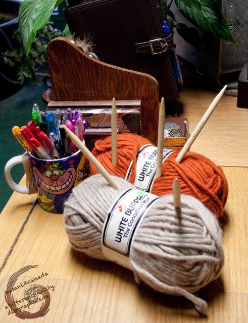 rainbow of pens in a Cheshire Cat mug bulky orange and light brown yarn and fat needles