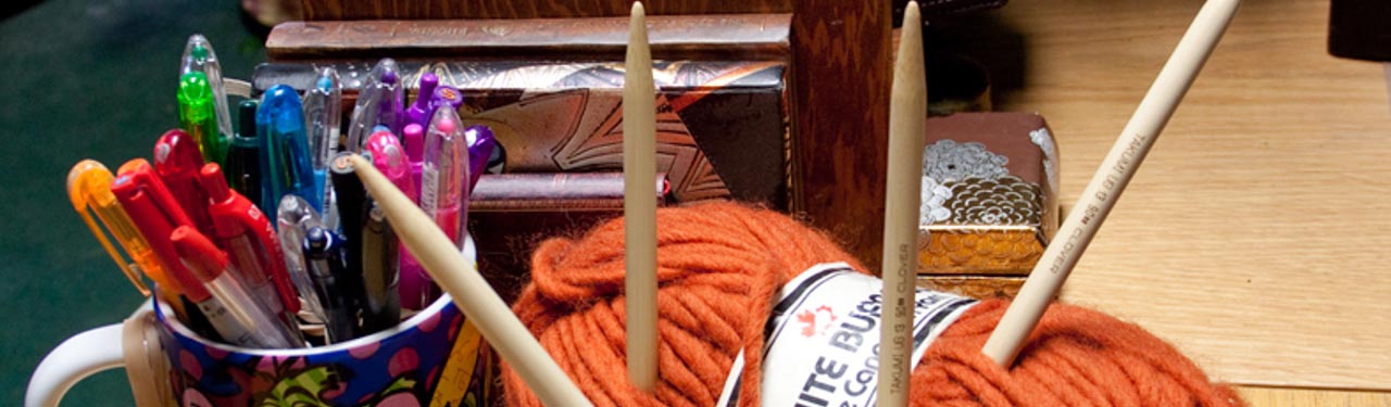 cropped image bulky orange yarn thick needles, mug with pens