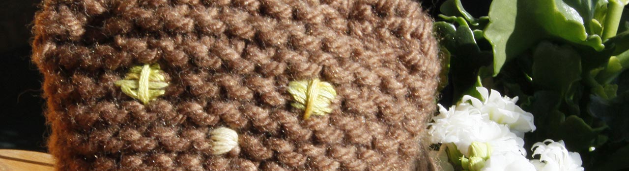 cat plush knit in brown yarn, white flowering plant behind