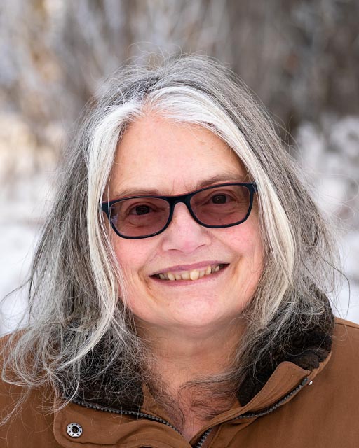 picture of smiling grey-haired lady with dark glasses, snowy background